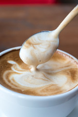 Closeup of someone using spoon to drink milk cream on the surface of Latte coffee.