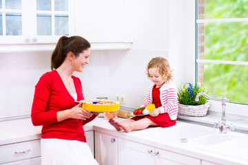 Beautiful young mother and daughter baking a pie