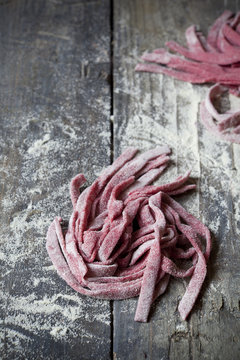 fresh pasta tagliatelle with beetroot on rustic table with flour