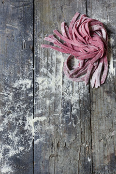 homemade pasta tagliatelle with beetroot on table with flour