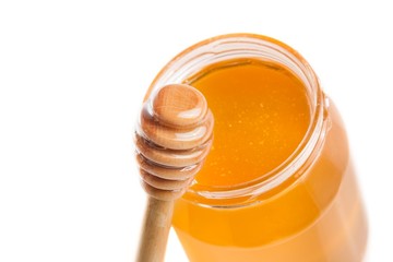opened honey jar on white background near wooden honey dipper
