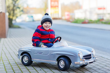 Happy little boy driving big toy car and having fun, outdoors
