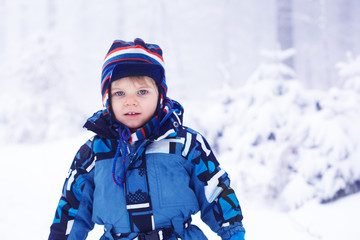 Fototapeta na wymiar Little toddler boy having fun with snow outdoors on beautiful wi