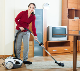 Happy mature woman cleaning with vacuum cleaner
