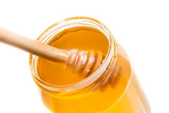 honey jar on white background with wooden honey dipper inside
