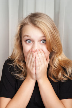 Beautiful blond Caucasian surprised girl covers her mouth