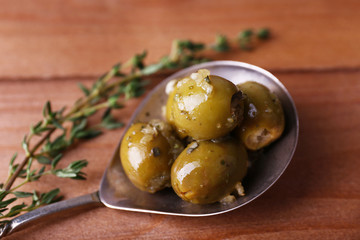 Green olives in oil with spices and rosemary in spoon