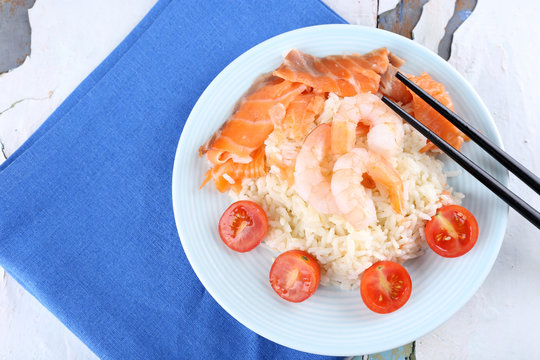 Boiled rice and shrimps, salmon on plate, on wooden background