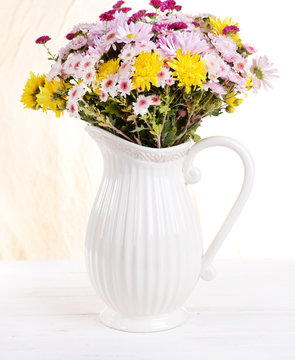 Beautiful flowers in pitcher on table on light background