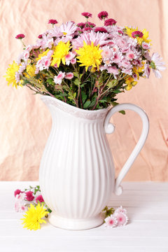 Beautiful flowers in pitcher on table on light background