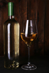 Wine bottle and wineglass with white wine on wooden background