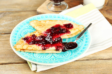 Delicious pancakes with berry jam on plate on wooden background
