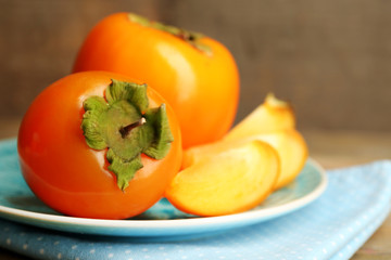 Ripe persimmons on plate, on wooden background