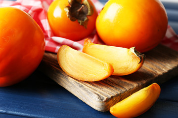 Ripe persimmons on cutting board, on color wooden background