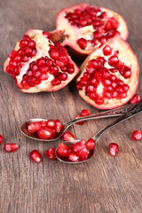 Juicy ripe pomegranates seeds in spoons, on old wooden table
