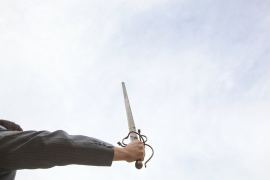 A Business Man In A Suit Holding A Sword High In The Sky