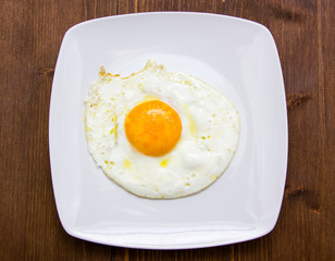 Fried egg on plate over wooden table from above