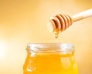honey jar on golden background with wooden dipper on top