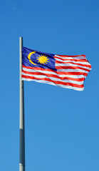 Флаг Малайзии на флагштоке на фоне голубого неба