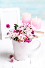 Beautiful flowers in cup on table on light blue background