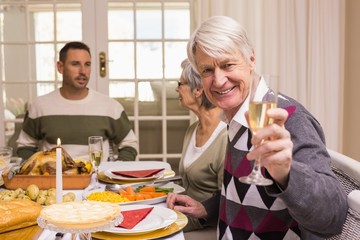 Smiling grandfather toasting at camera in front of his family