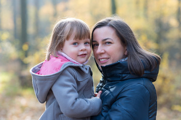 Mother holding daughter in autumnal forest smiling