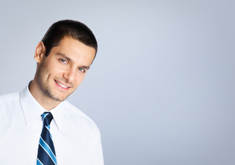 Happy smiling young businessman, against grey