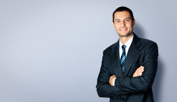 Happy businessman with crossed arms, against grey