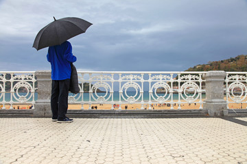 san sebastián donostia hombre con paraguas mirando a la playa de la concha desde la barandilla...