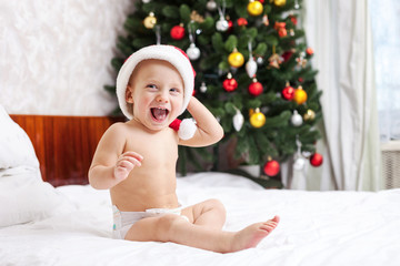Obraz na płótnie Canvas Christmas baby in santa hat sitting on bed and laughing