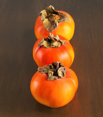 Three ripe persimmon on the wooden background
