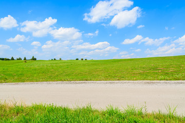 Fototapeta premium Road in green fields with white clouds on sunny blue sky, Poland