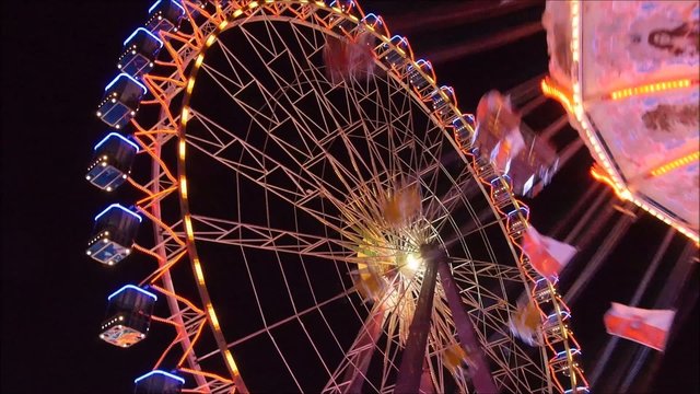 Buntes leuchtendes Riesenrad und drehendes Ketten-Karusell mit Fahnen in Bewegung bei Nacht auf einer Kirmes, Volksfest, Rummel mit Lichtern
