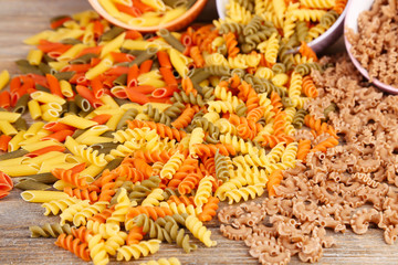 Assortment of colorful pasta in color bowls on wooden