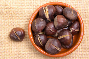 Roasted chestnuts in bowl on placemat jute top views
