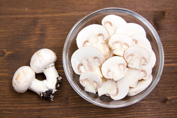 Sliced mushrooms in bowl on wooden table seen from above
