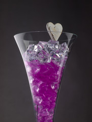 Glass of champagne filled with purple hearts and ice crystals.