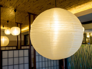 Warmly colored balloon white paper lanterns hanging from the ceiling inside of building, decoration.