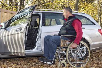 Man in a wheelchair in the fall next to their car