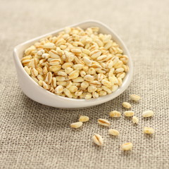 Wheat grains in white ceramic bowl on sackcloth background