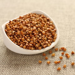 Buckwheat grains in white ceramic bowl on sackcloth background