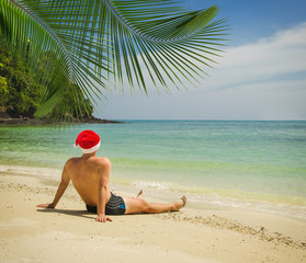 Man on the tropical beach in Santa Claus hat