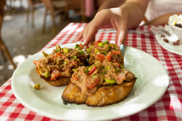 woman taking bruschetta with tuna from plate at restaurant