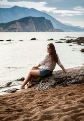 woman relaxing sitting on big rock on beach and looking at far a