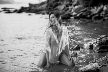 Monochrome photo of sexy young woman kneeling at sea shore