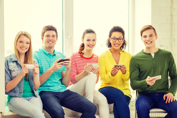 Obraz premium smiling students with smartphone texting at school