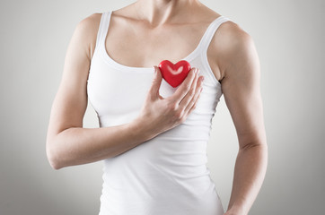 Close-up of female' body holding red heart at breast.