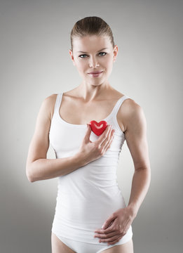 Smiling female holding red heart at breast. Heart protect