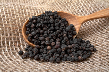 Black pepper in wooden spoon on burlap background