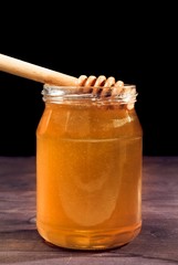 honey jar on wood table and black background with wood dipper